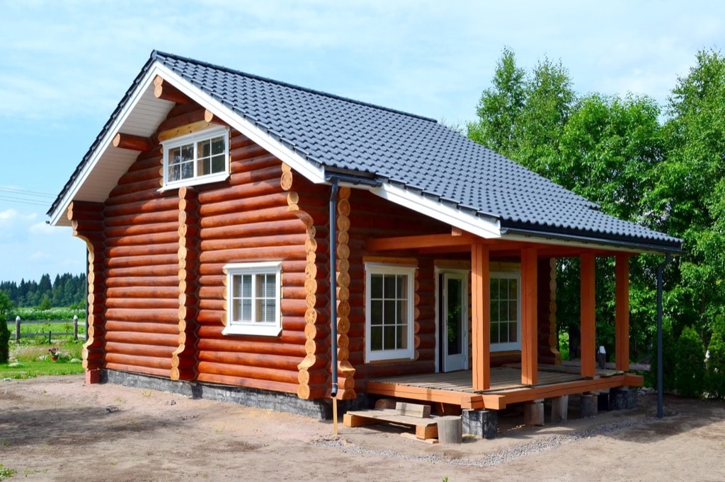 Фасад деревянного дома из рубленного бревна (сосна) с террассой. Крыша металлочерепица серого цвета.